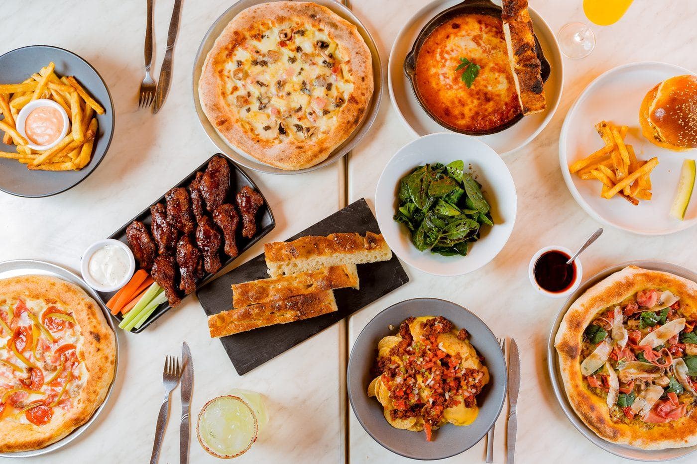 Mesa completa con pizzas, alitas, papas y pan